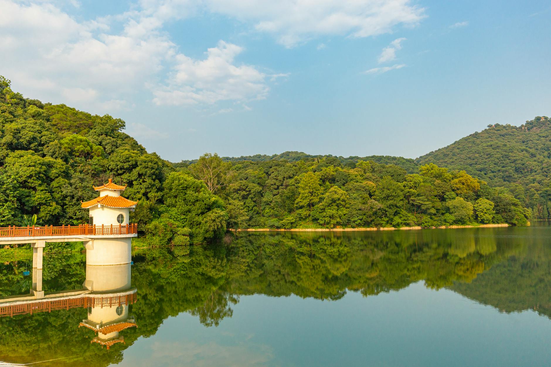 Serene landscape featuring a reflective lake and pagoda surrounded by lush greenery under a clear sky.
