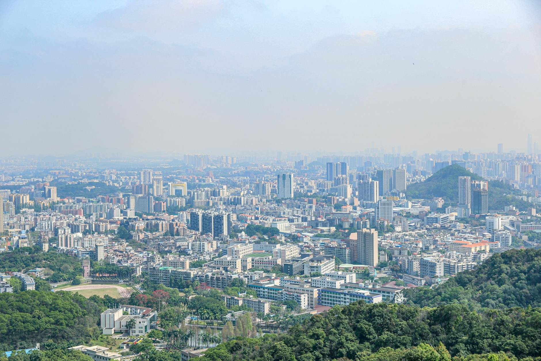 Aerial view of a sprawling city showing dense architecture and greenery under a clear blue sky.