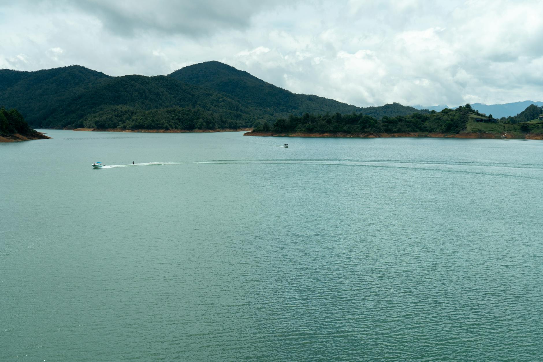 Scenic view of boats on Guatapé Reservoir surrounded by lush hills under a cloudy sky.