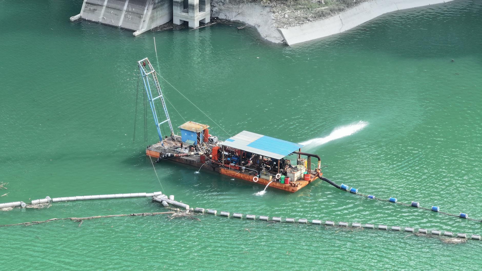 Dredging barge operating on a pristine aqua-colored lake, photographed from above.