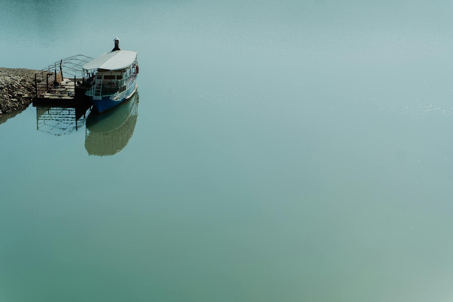 A lone boat docked by a quiet shore, reflecting its serene presence on calm, blue waters.