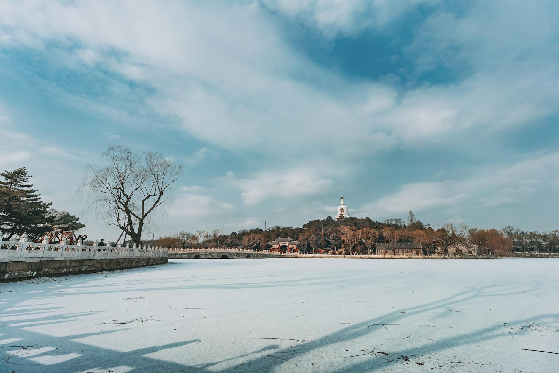 Winter landscape of Beihai Park in Beijing with frozen lake and cloudy sky.
