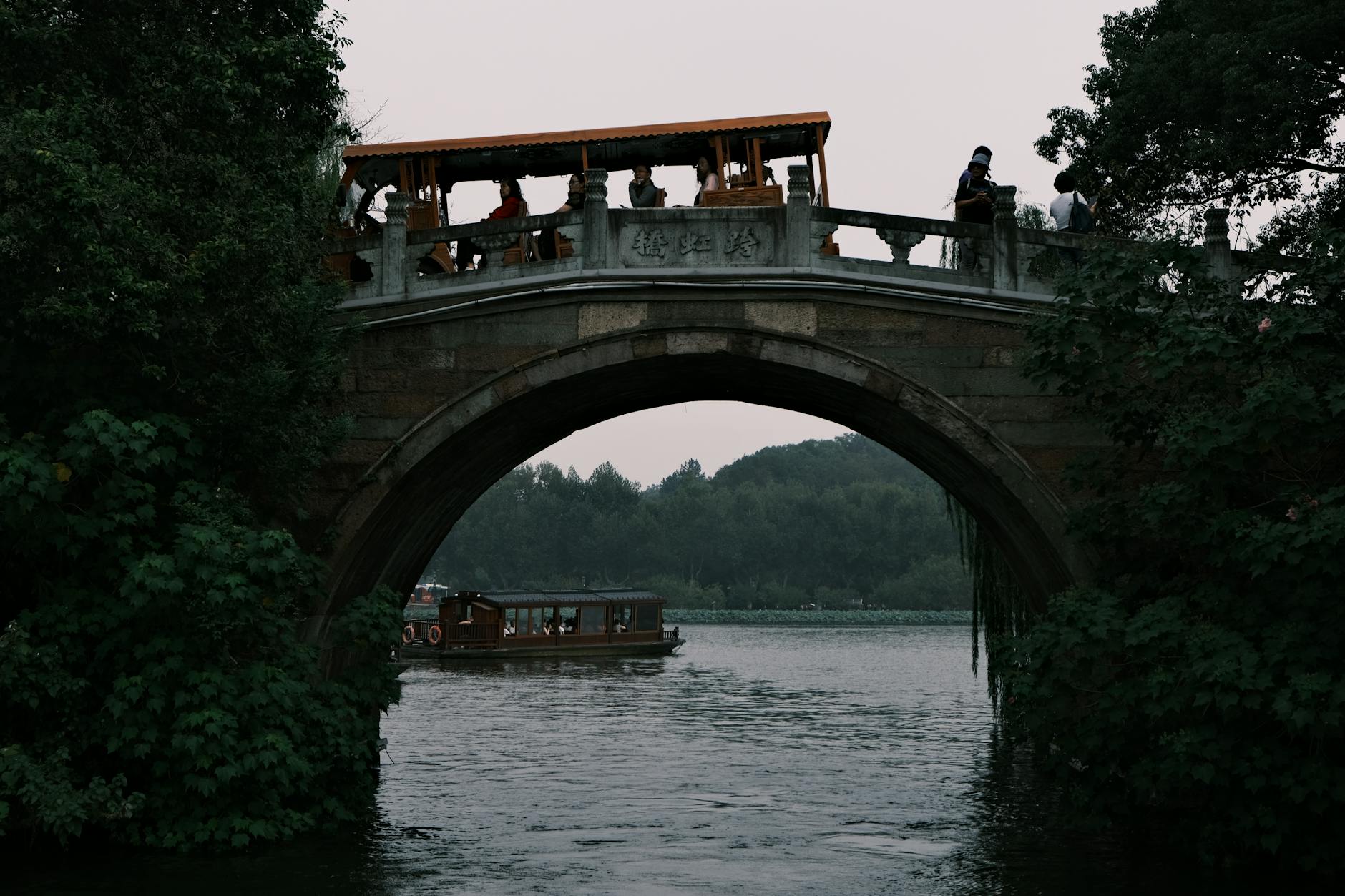 A peaceful scene of a traditional stone bridge with tourists and a boat beneath in Hangzhou, China.