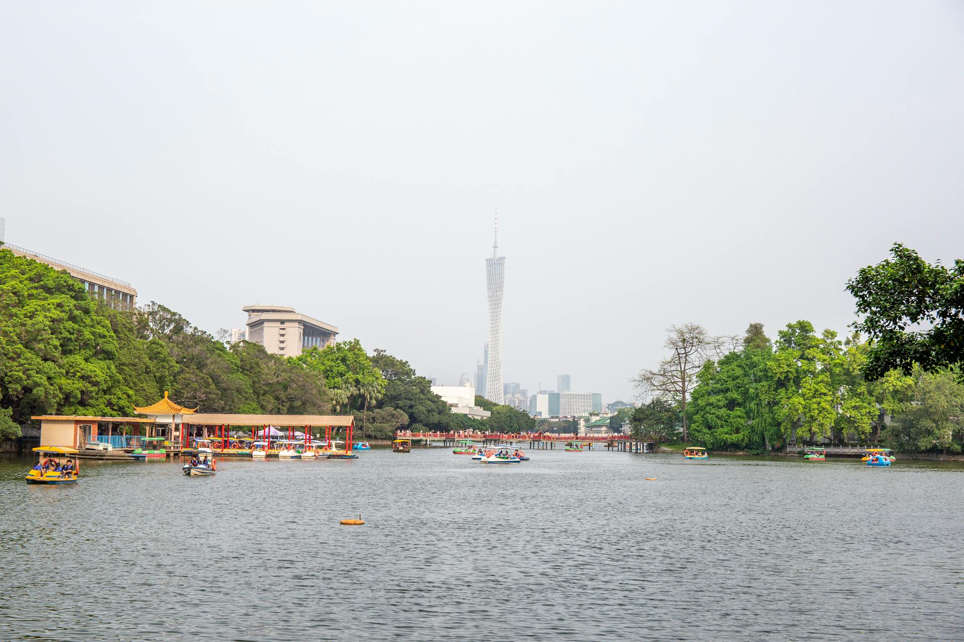 Idyllic view of Canton Tower with pedalos on the river in Guangzhou, China, surrounded by lush greenery.