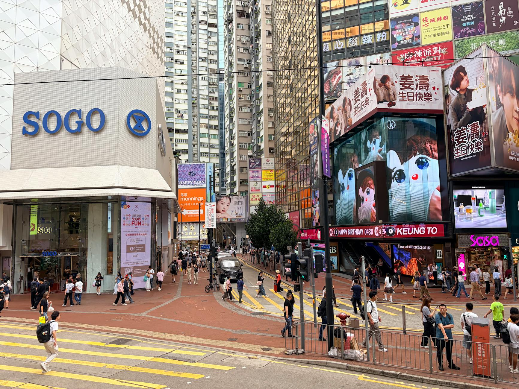 Vibrant city scene depicting a busy street near Sogo Department Store in Hong Kong, with digital billboards and pedestrians.