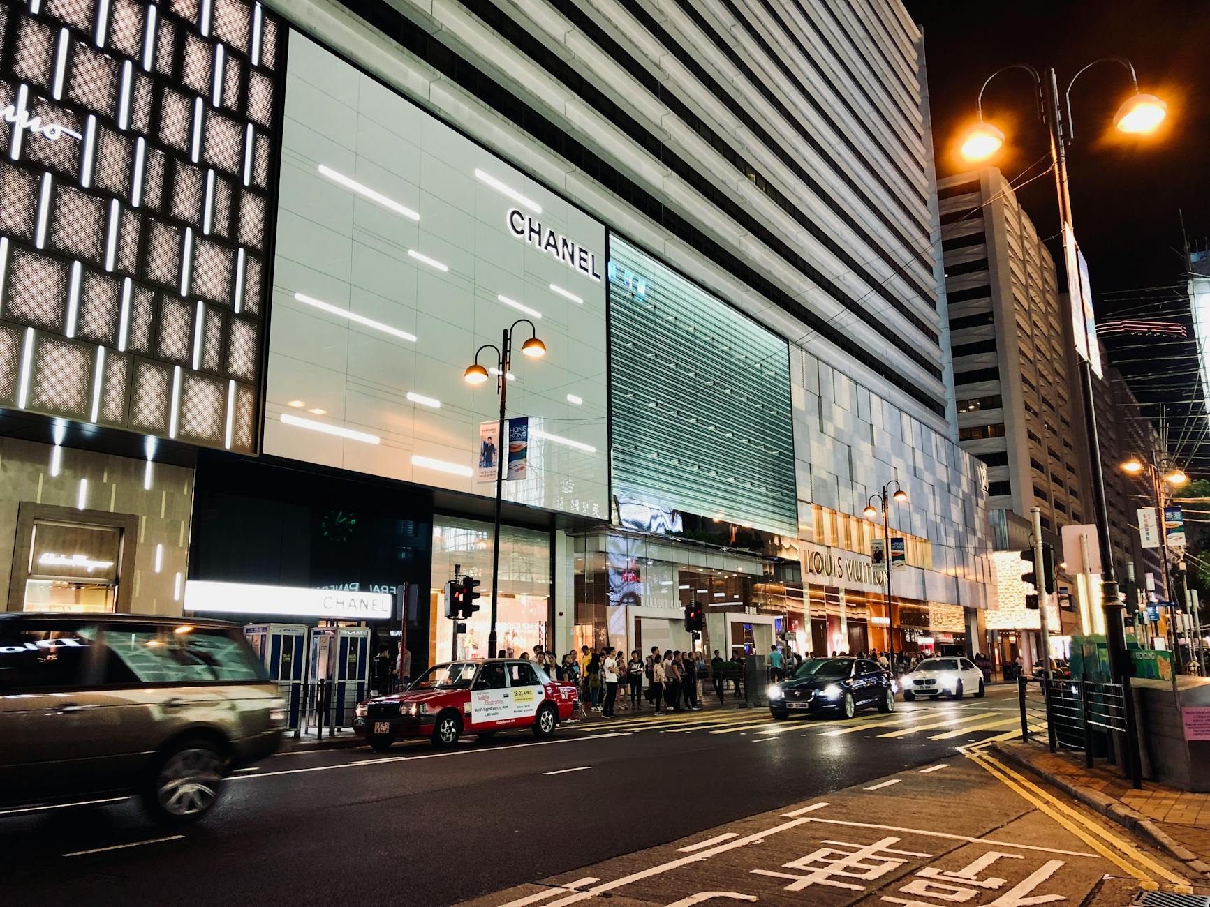 Vibrant nightlife scene capturing cars and people in Kowloon's shopping district, Hong Kong.