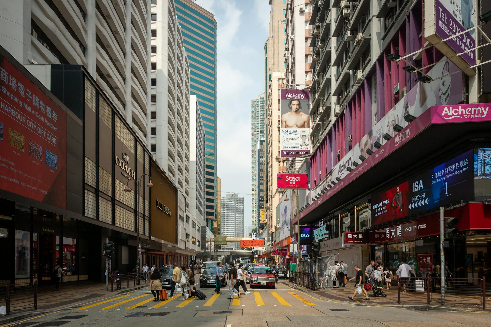 Vibrant and bustling street view in Hong Kong with pedestrians crossing and tall buildings around.
