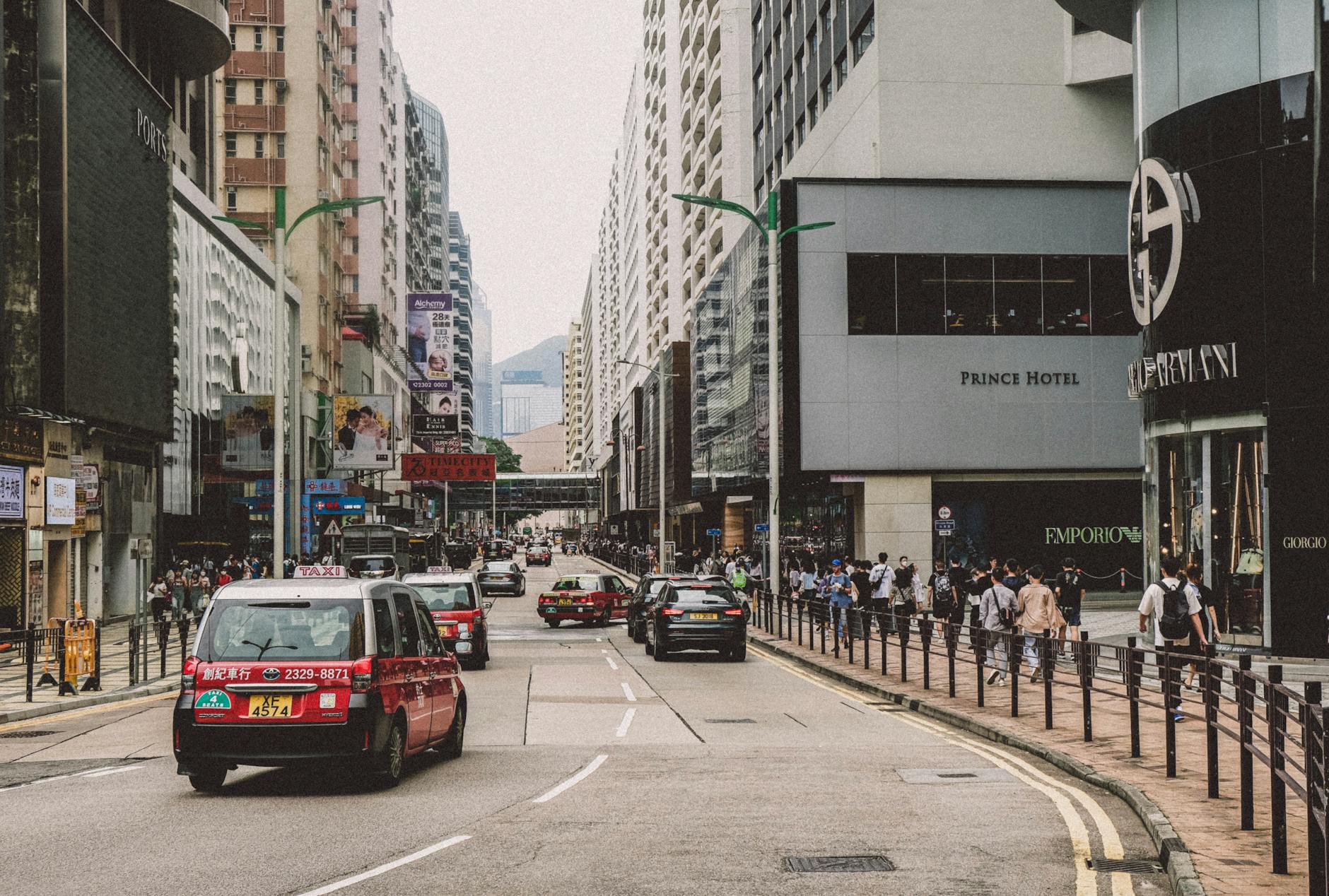 A vibrant city street scene with bustling traffic and busy sidewalks, featuring urban architecture.