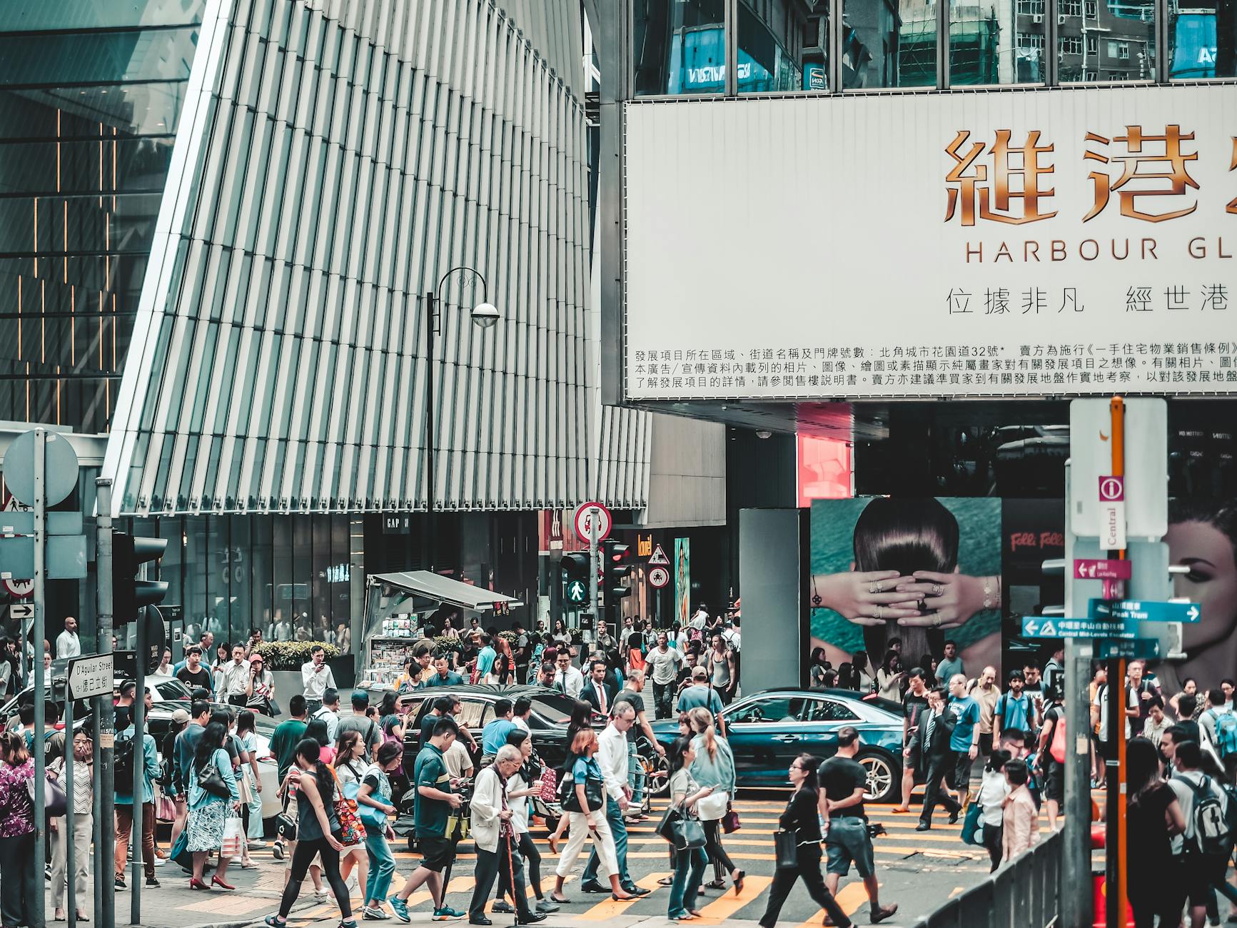 Crowd of people crossing street in busy Hong Kong shopping district under large signs.