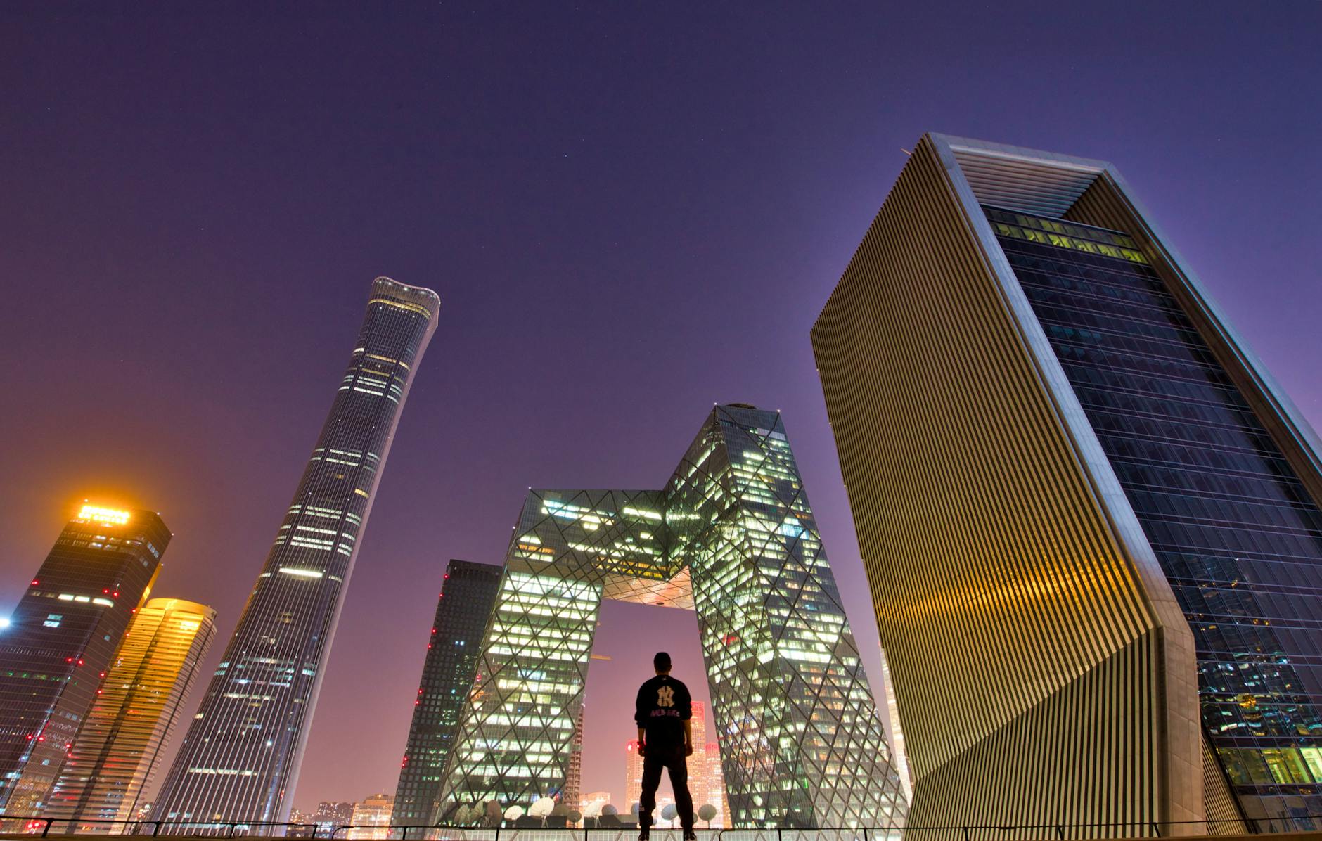 Silhouette of a man overlooking Beijing's skyline at twilight. Modern architecture in focus.