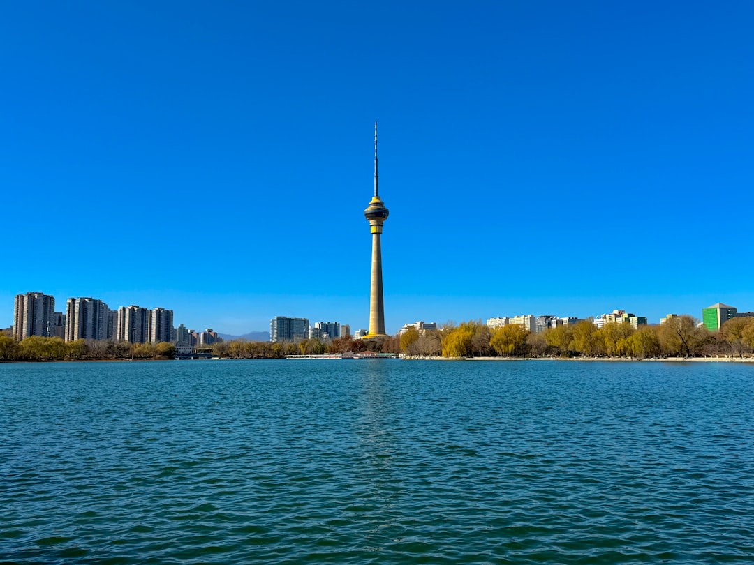 Tall tower stands by a lake with city buildings.