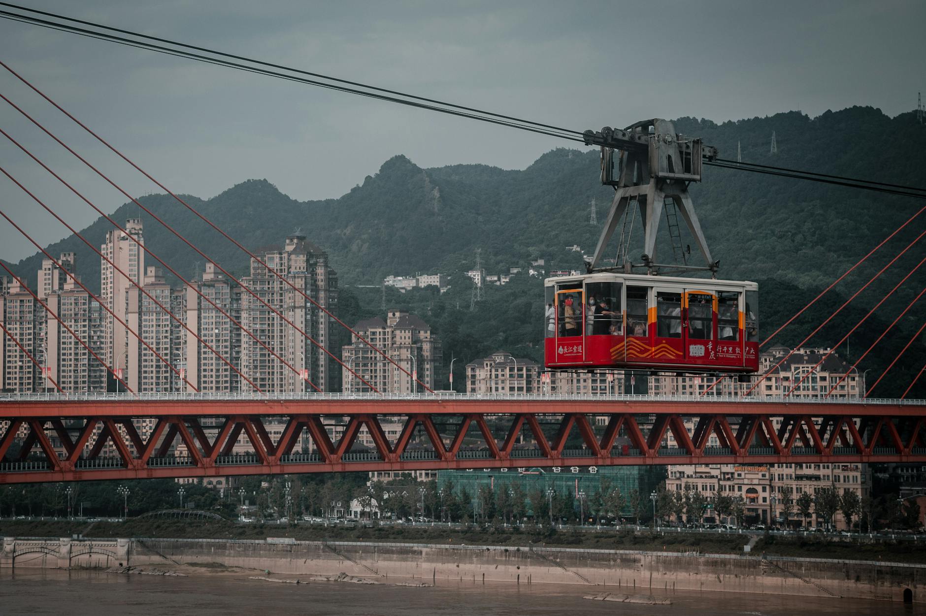 Urban cityscape featuring a cable car crossing over a bridge in Chongqing, China with a backdrop of high-rise buildings.