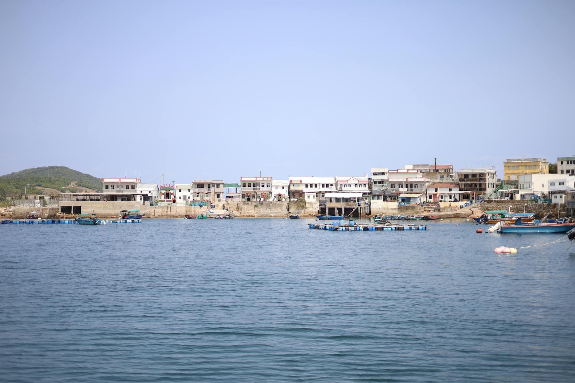 Scenic view of a fishing village along the Hong Kong coast with small boats and clear skies.