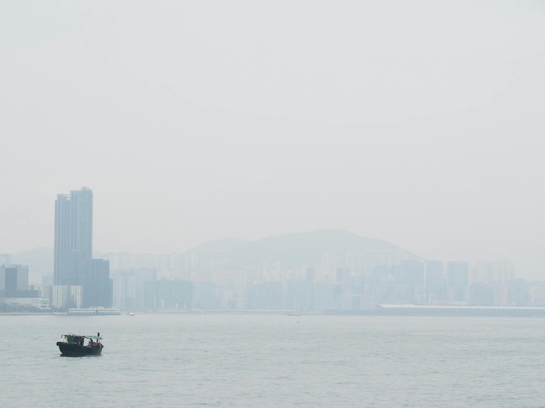 Tranquil view of a boat on foggy Hong Kong harbor with distant city skyline.