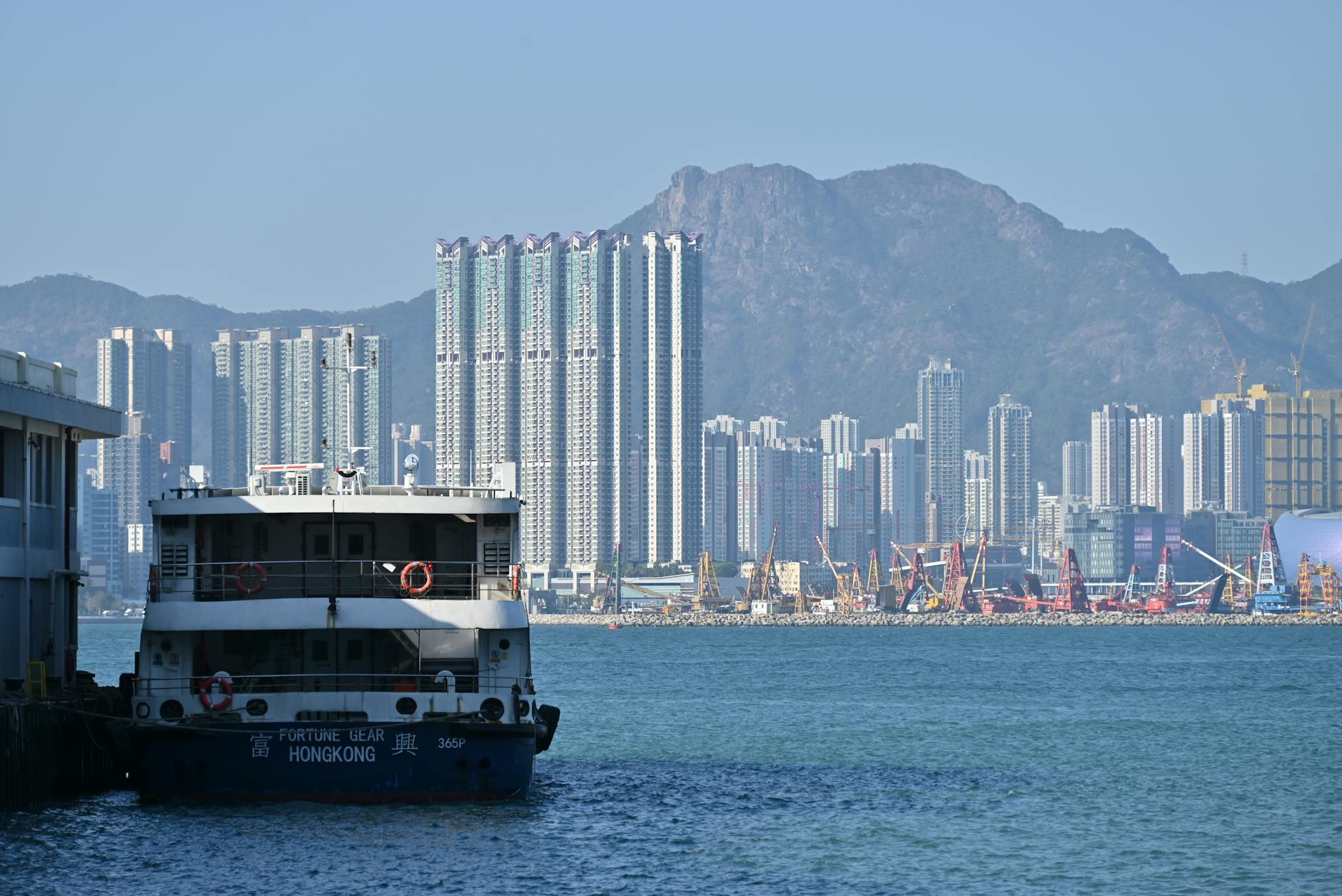 A ferry docked at Hong Kong harbor with a backdrop of modern skyscrapers and hills.