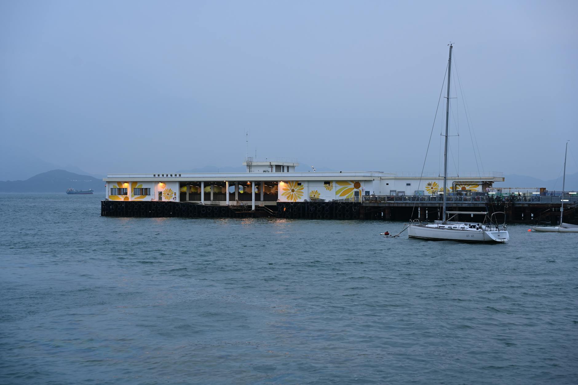A serene view of a pier in Hong Kong with a sailboat at twilight, surrounded by calm waters.