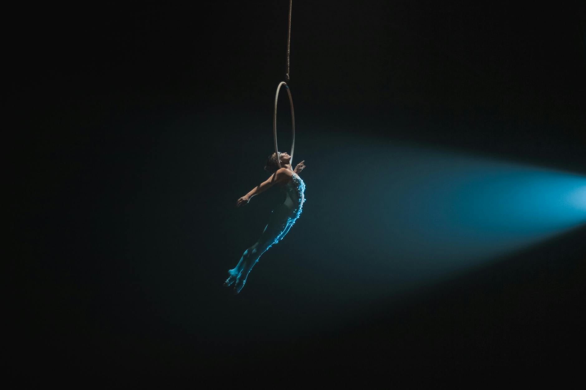 A captivating aerial artist performs gracefully on a hoop, illuminated by a spotlight in a dark setting.