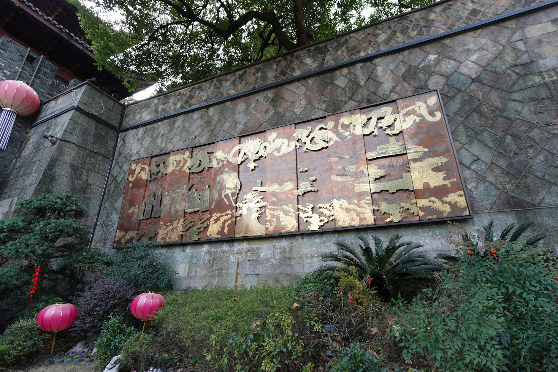 A detailed wall art installation surrounded by lush greenery in Hangzhou, capturing the essence of traditional Chinese design.