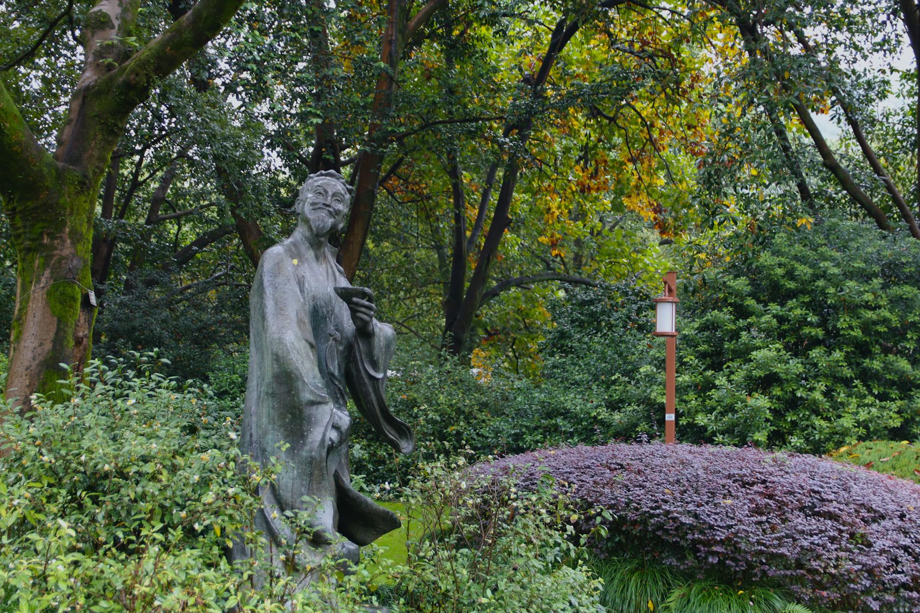 A peaceful garden featuring a traditional Chinese statue surrounded by lush greenery.