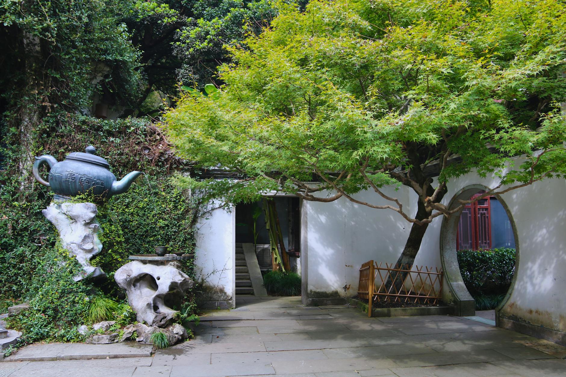 Tranquil courtyard with teapot sculpture and lush greenery in Hupao Park, Hangzhou, China.