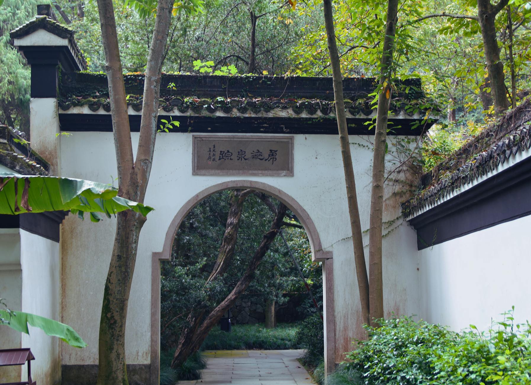 Charming white archway surrounded by lush greenery in Hangzhou's Hupao Park.