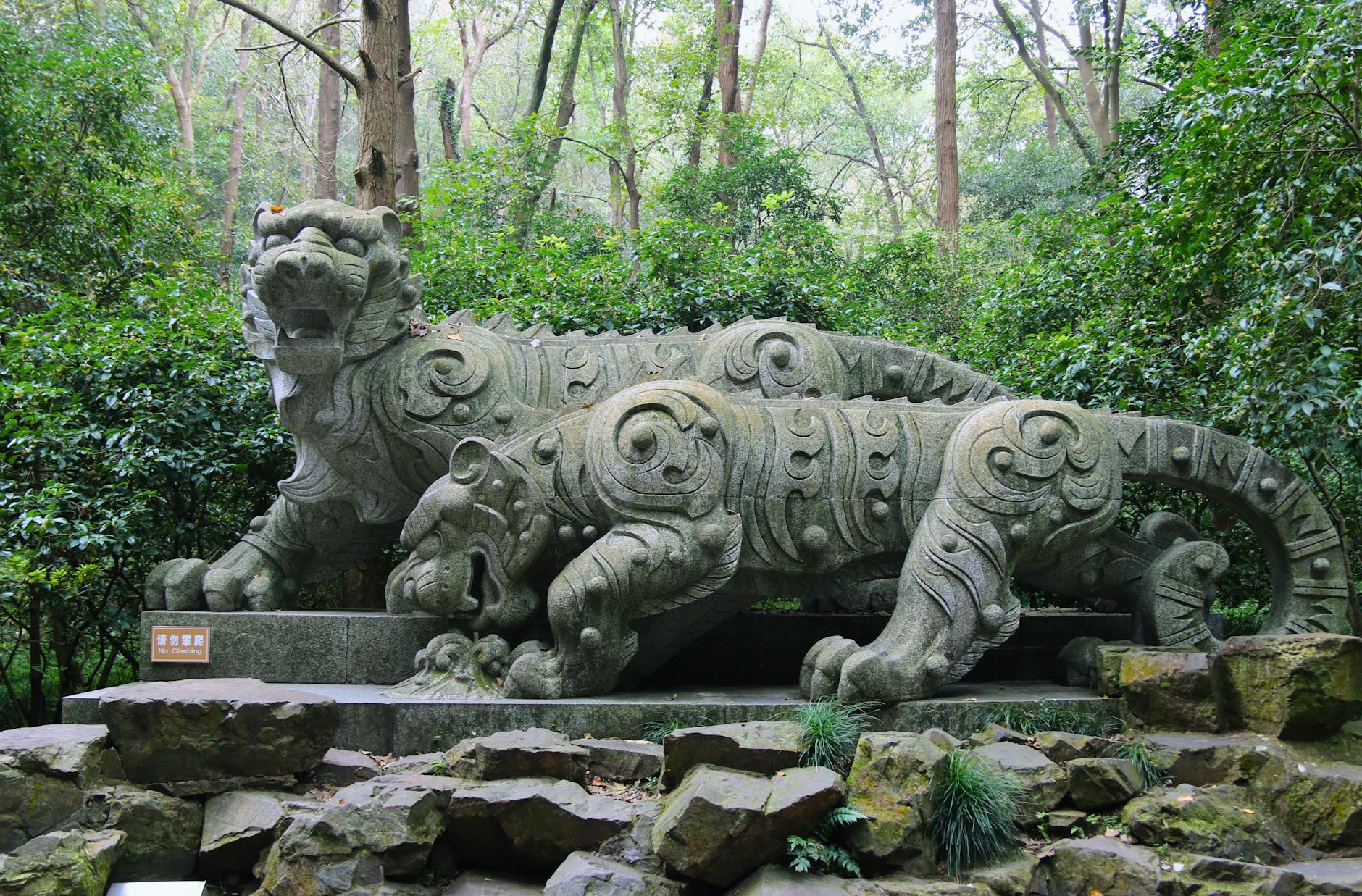 Intricate stone tiger sculptures in Hupao Park, Hangzhou, surrounded by lush greenery.