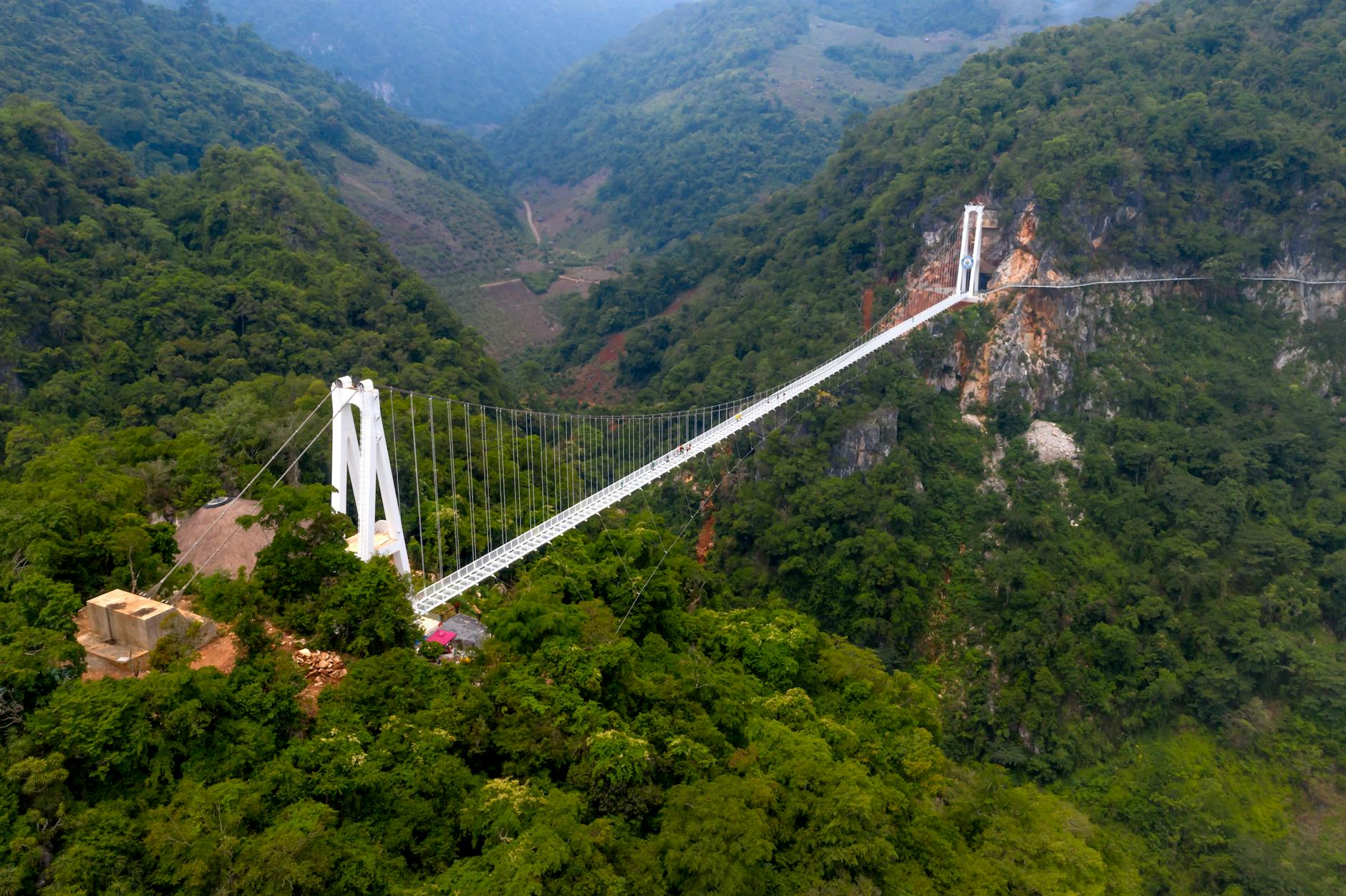 Breathtaking suspension bridge spans a lush, mountainous valley, captured from above.