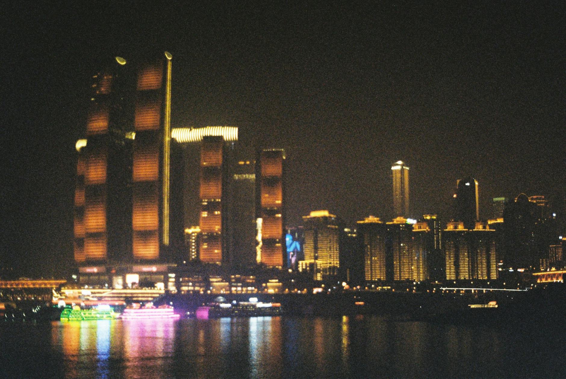 Illuminated Chongqing skyline with modern skyscrapers reflecting off the river at night.