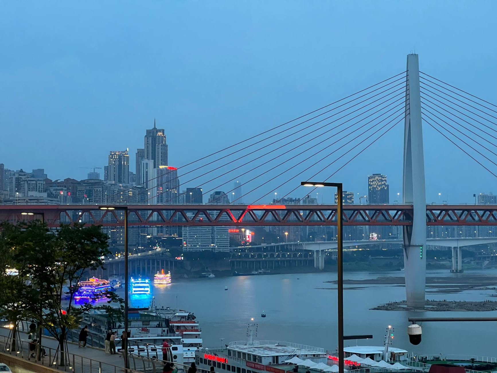 Aerial view of Chongqing at dusk with Qiansimen Bridge and illuminated skyline.