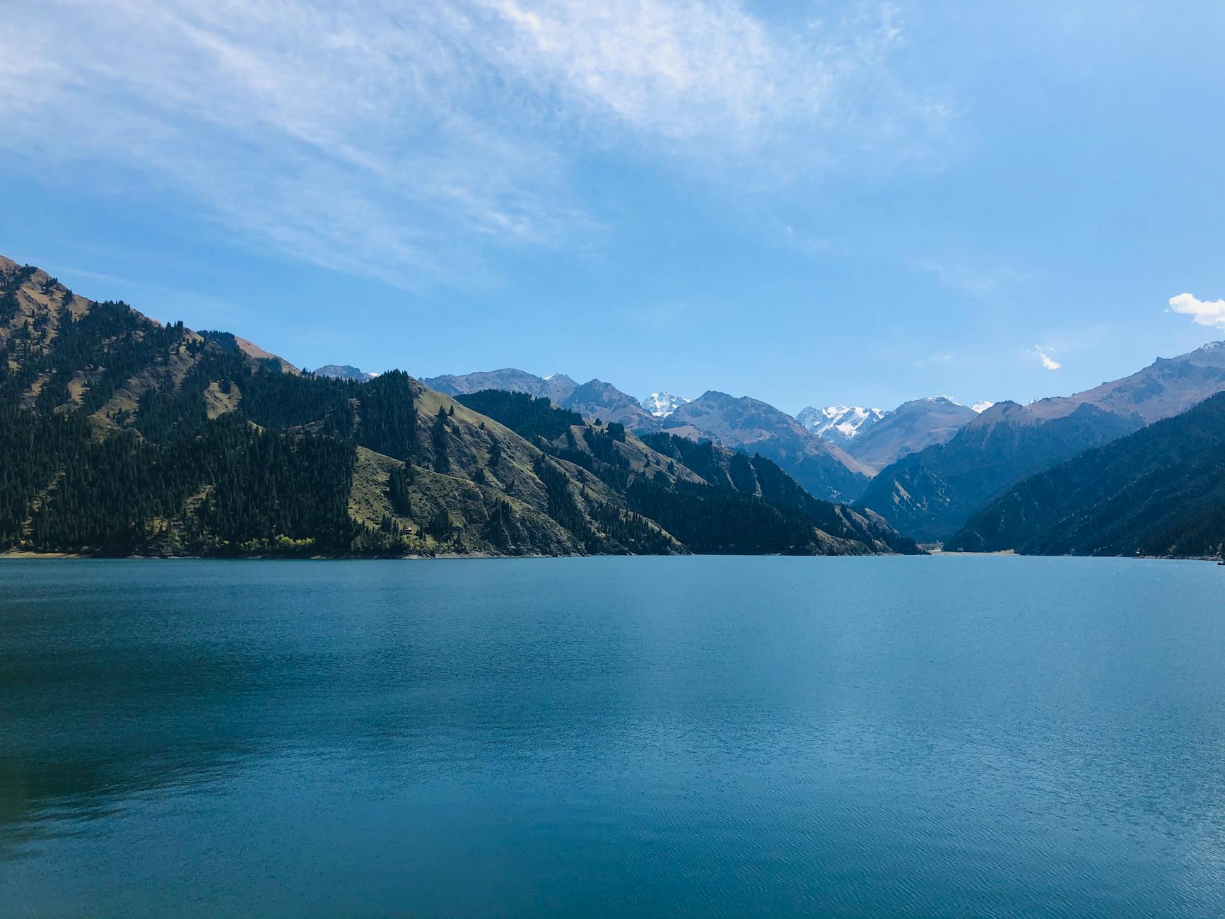 Breathtaking scenery of clear lake with mountainous backdrop under blue sky in Xinjiang, China.