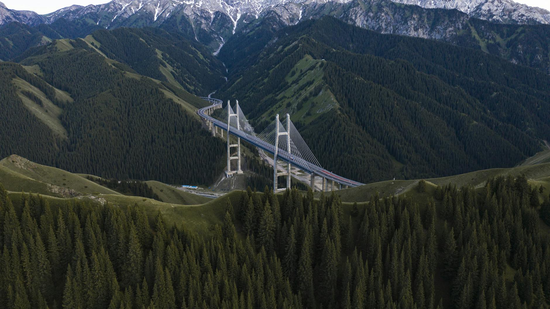 A breathtaking aerial view of the Guozigou Bridge set amidst Xinjiang's majestic mountain ranges.