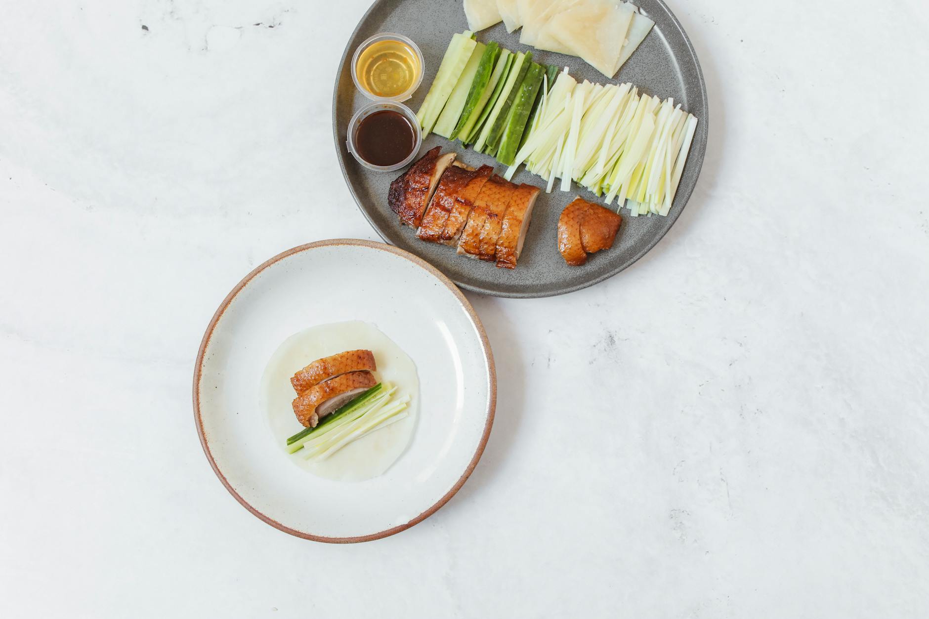 Delicious Peking duck served with fresh cucumbers, scallions, and classic sauces on a white table.