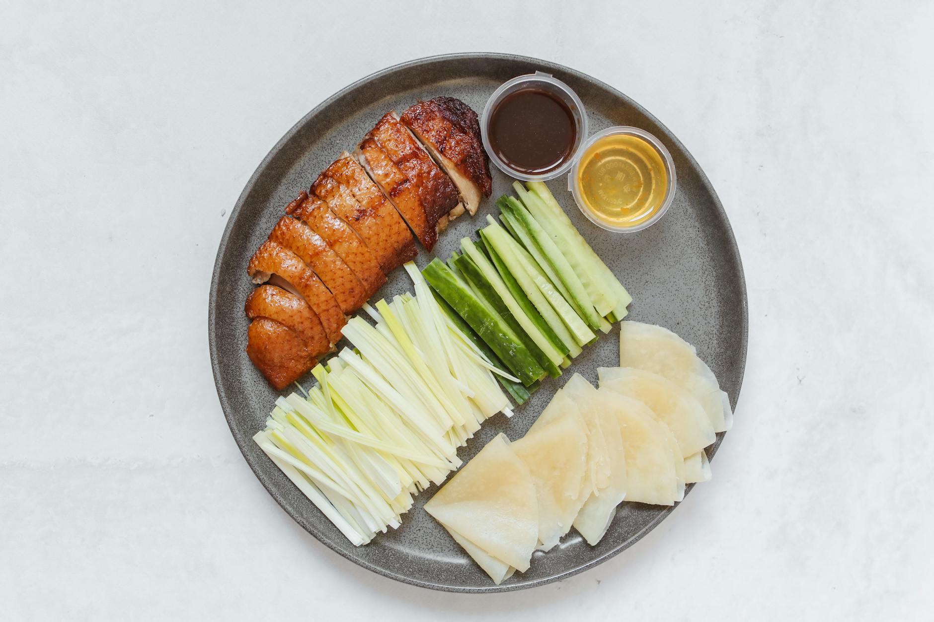 Plate of traditional Peking duck served with cucumbers, onions, hoisin, and pancakes, ready for rolling.