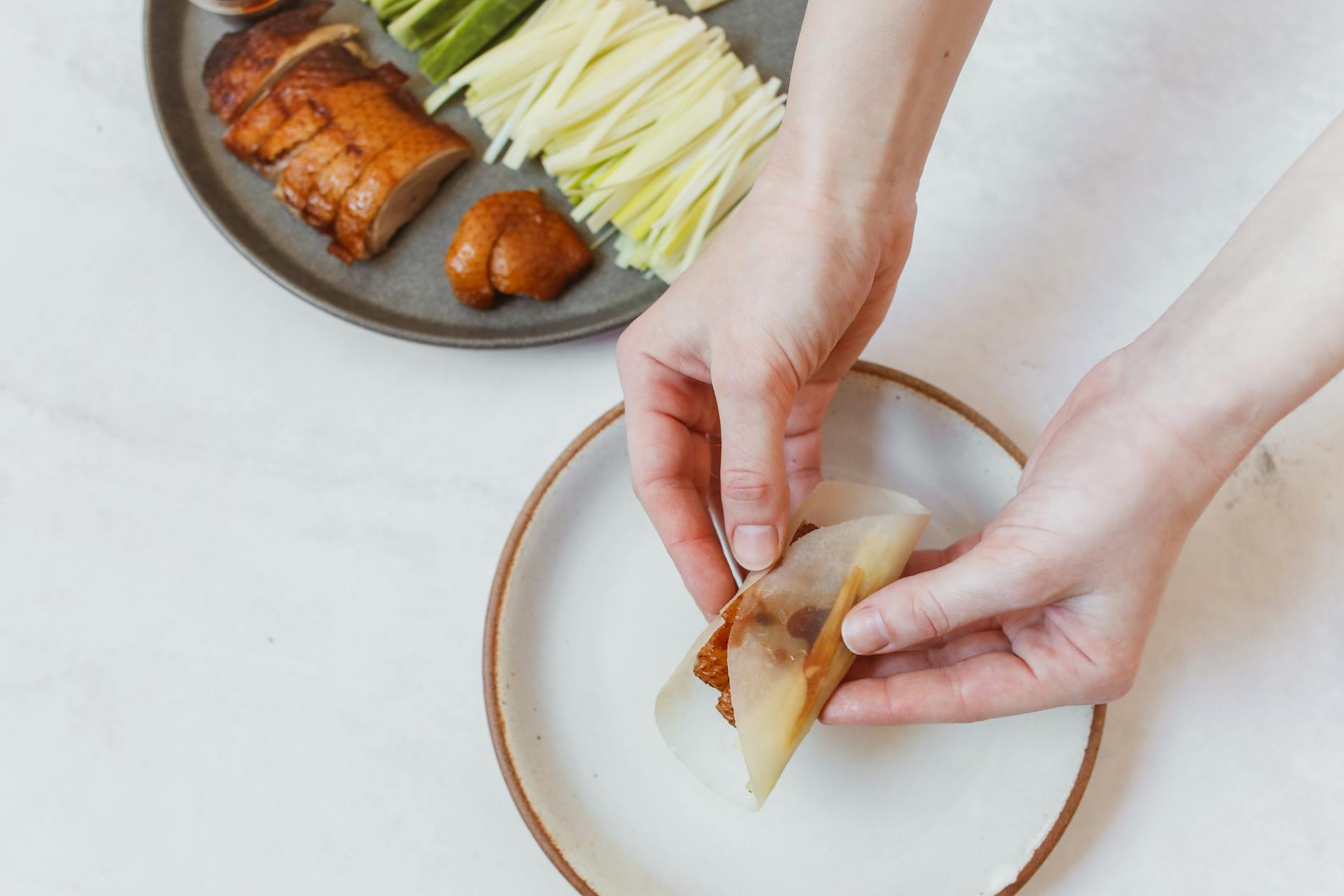 Close-up of hands wrapping Peking duck with vegetables on a plate. Traditional Chinese cuisine.