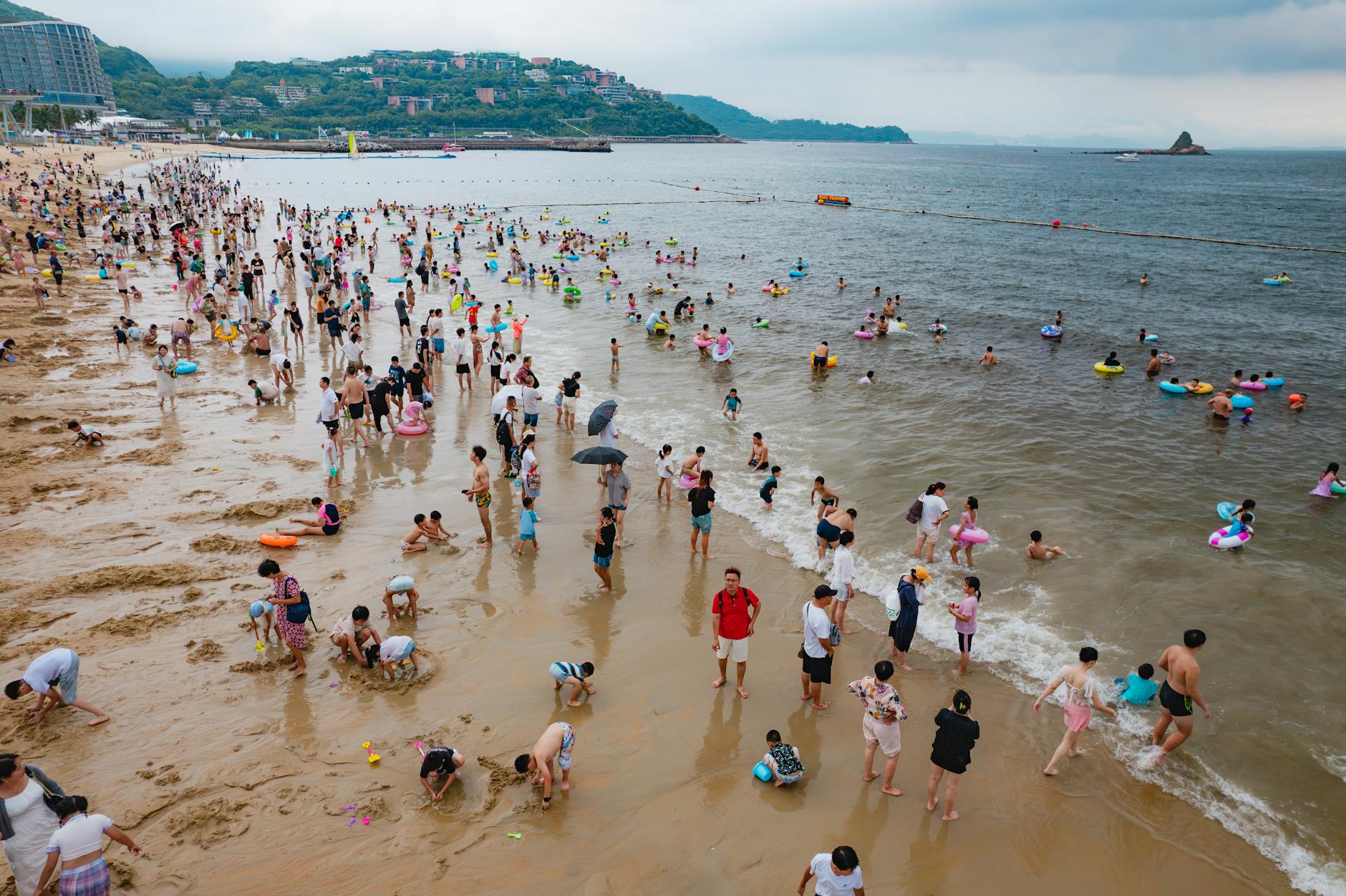 A lively scene at Dameisha Beach, Shenzhen, with people enjoying summer leisure activities by the sea.
