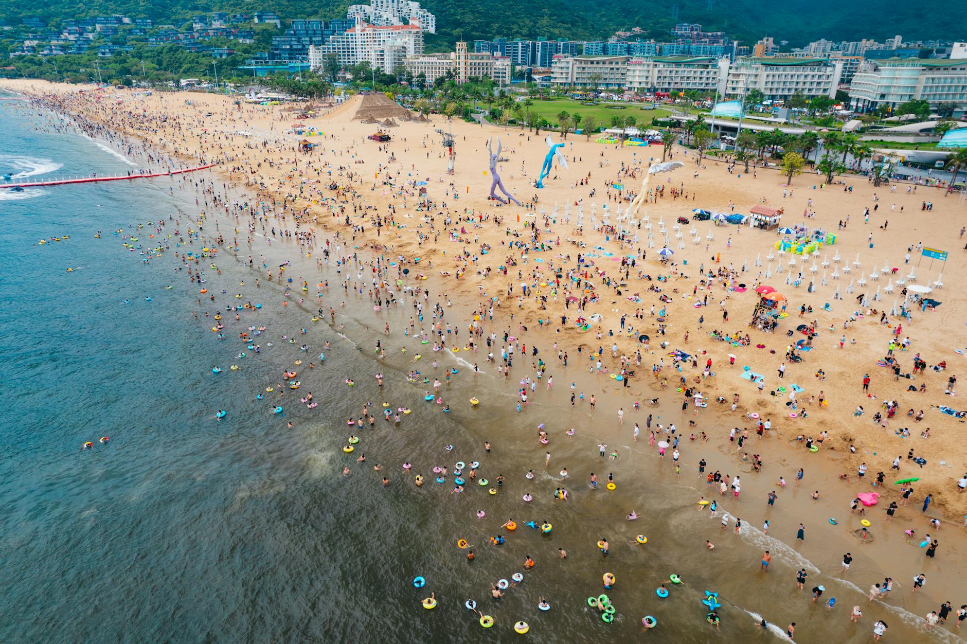 A lively summer day at a crowded beach in Shenzhen, China, featuring vibrant activities and scenic views.