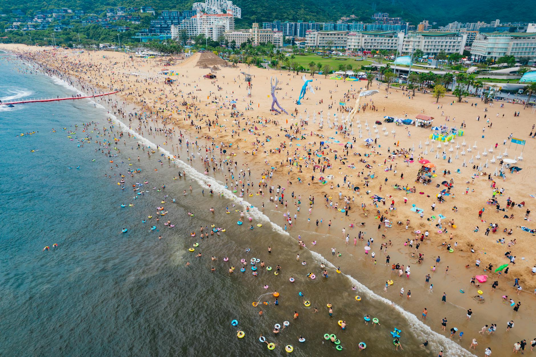Aerial view of a crowded beach in Shenzhen, China, with colorful umbrellas and swimmers.
