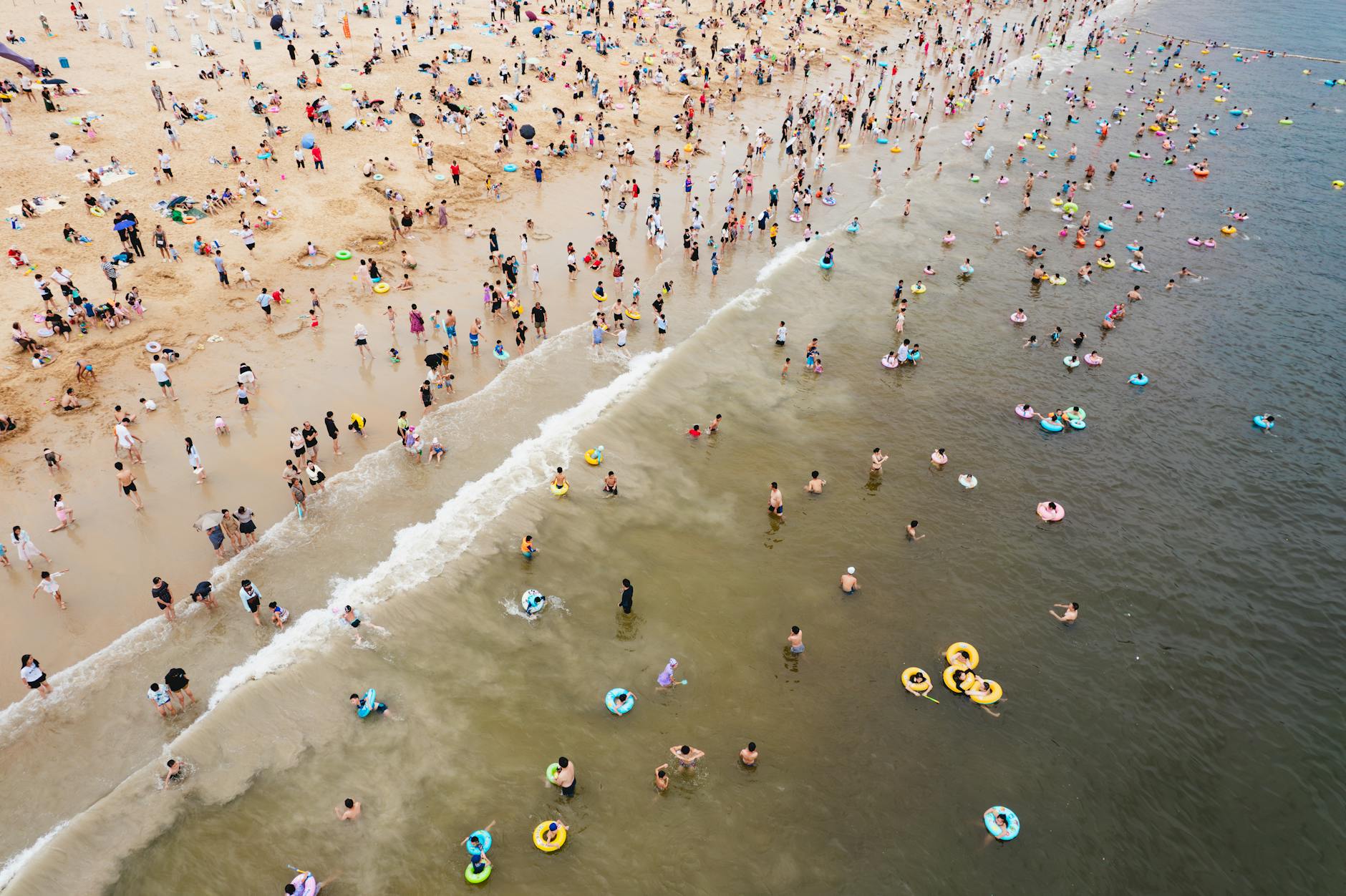 A vibrant summer scene at a crowded beach in Shenzhen, China, teeming with people enjoying the sun and sea.