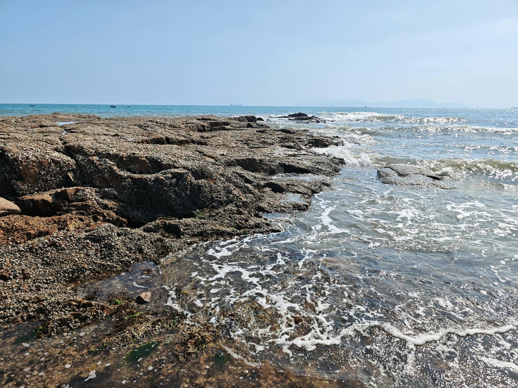 A sunlit rocky shoreline with gentle ocean waves under a clear sky, perfect for nature and travel themes.