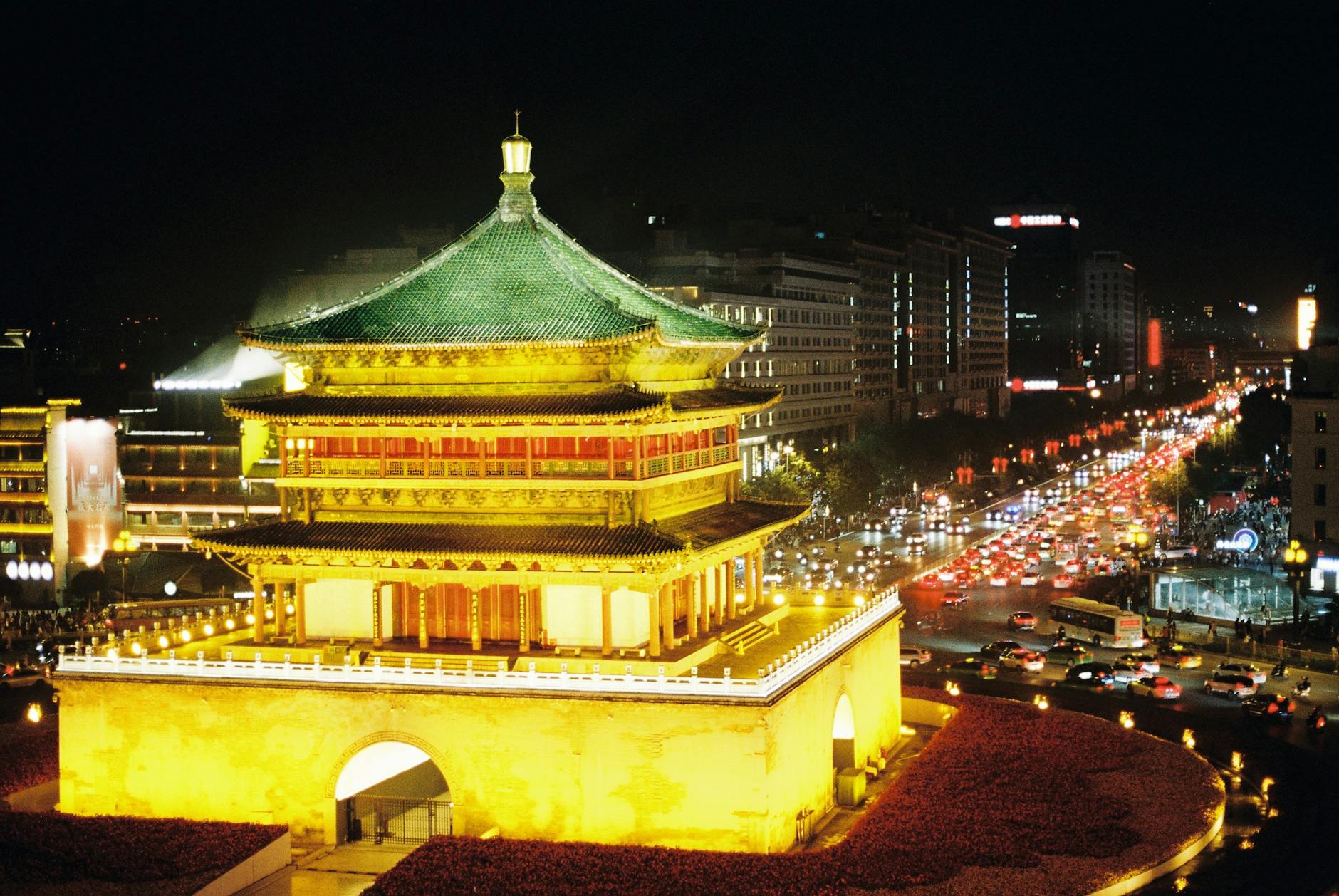 A stunning night view of the illuminated Bell Tower in Xi'an, showcasing vibrant urban life.