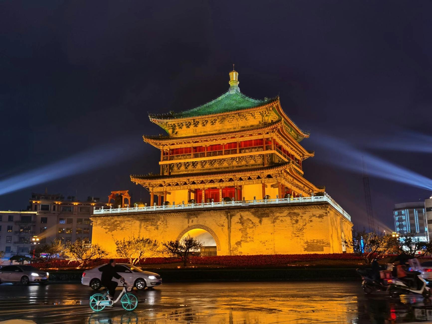 A stunning nighttime view of an illuminated historical landmark in China with wet roads and moving cars.
