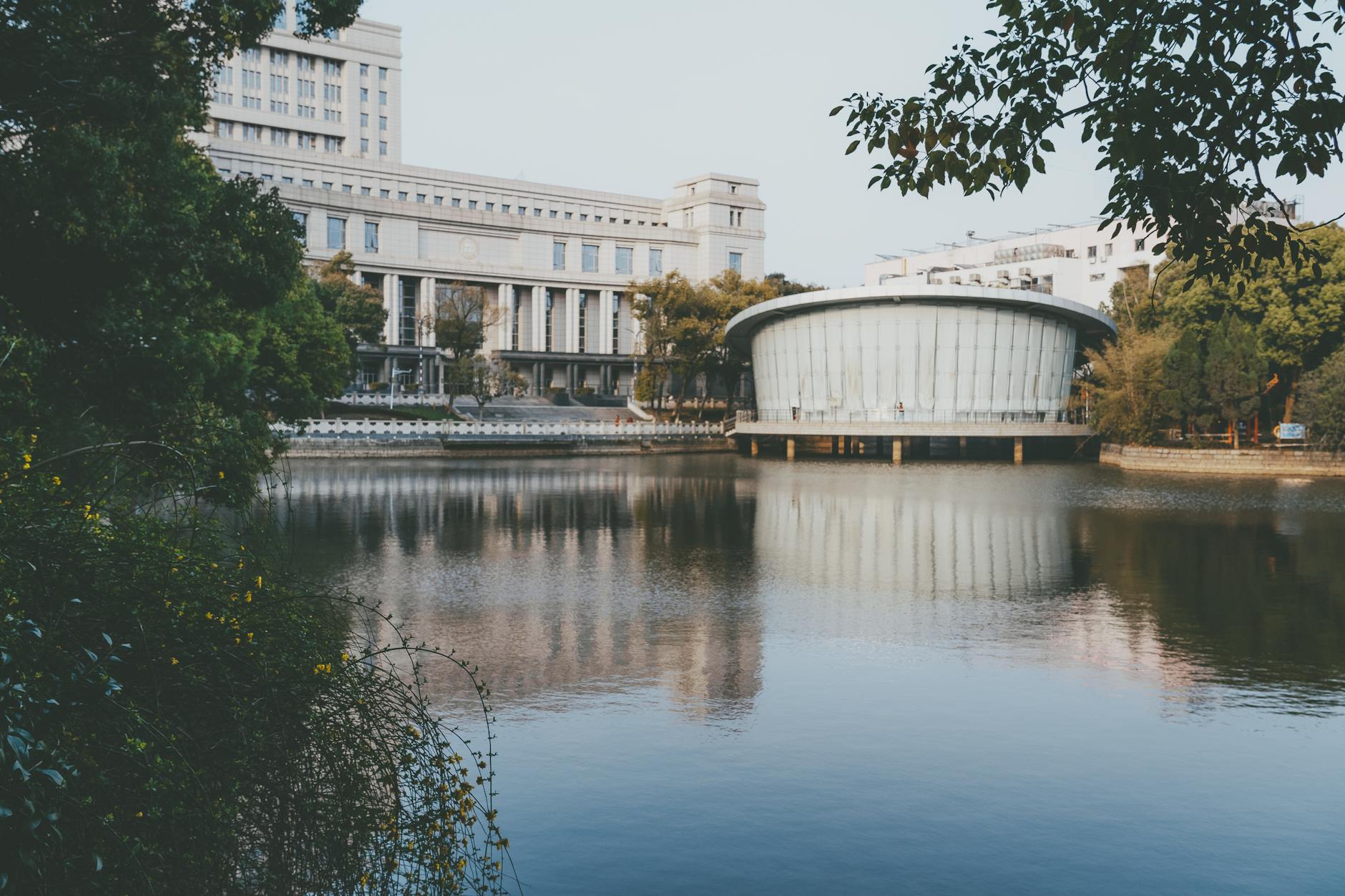 Peaceful lake reflecting modern architecture amidst lush greenery in an urban setting.