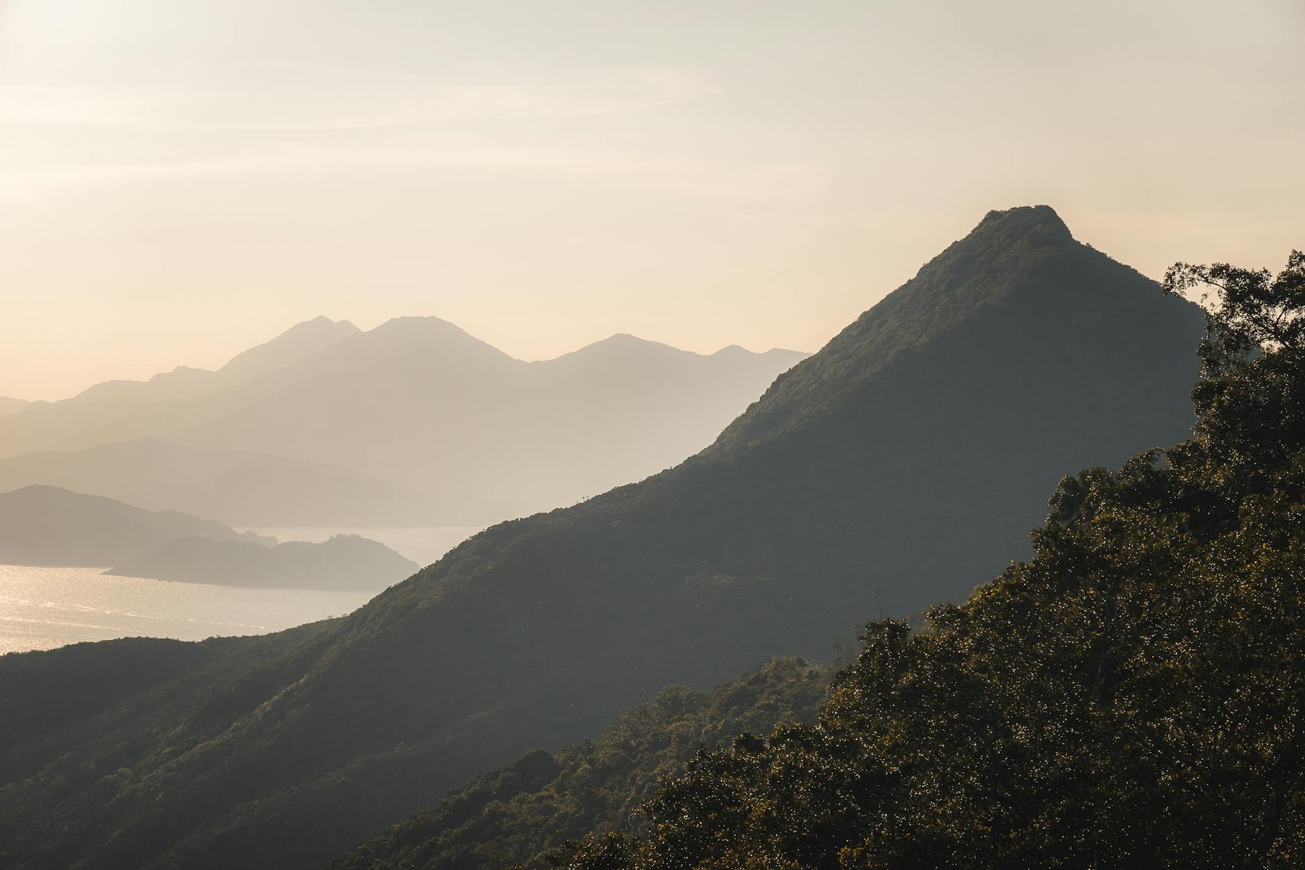 A tranquil view of Hong Kong Island's mountains at sunset, featuring layered silhouettes and a warm glow.