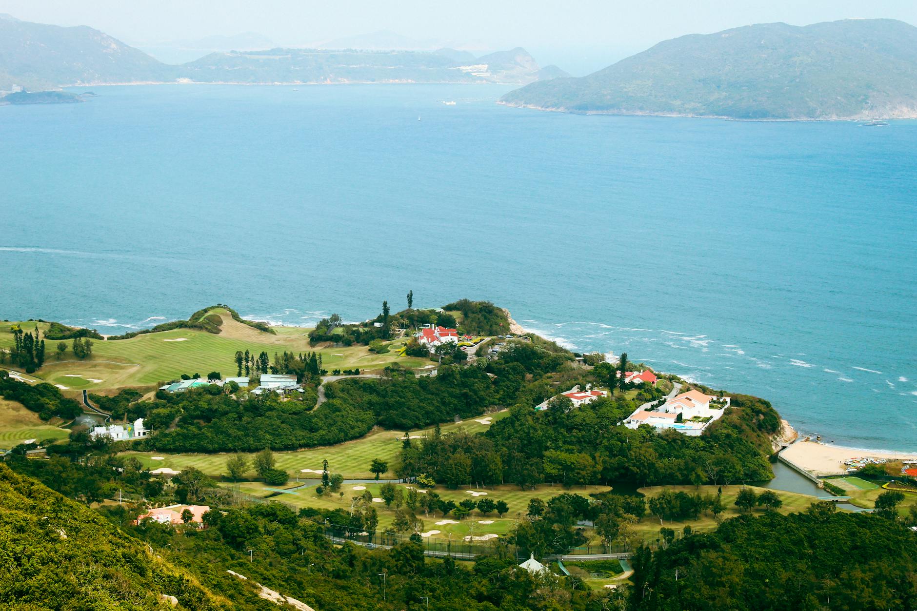 Aerial view of a scenic coastal golf course in Hong Kong, surrounded by lush greenery and the ocean.