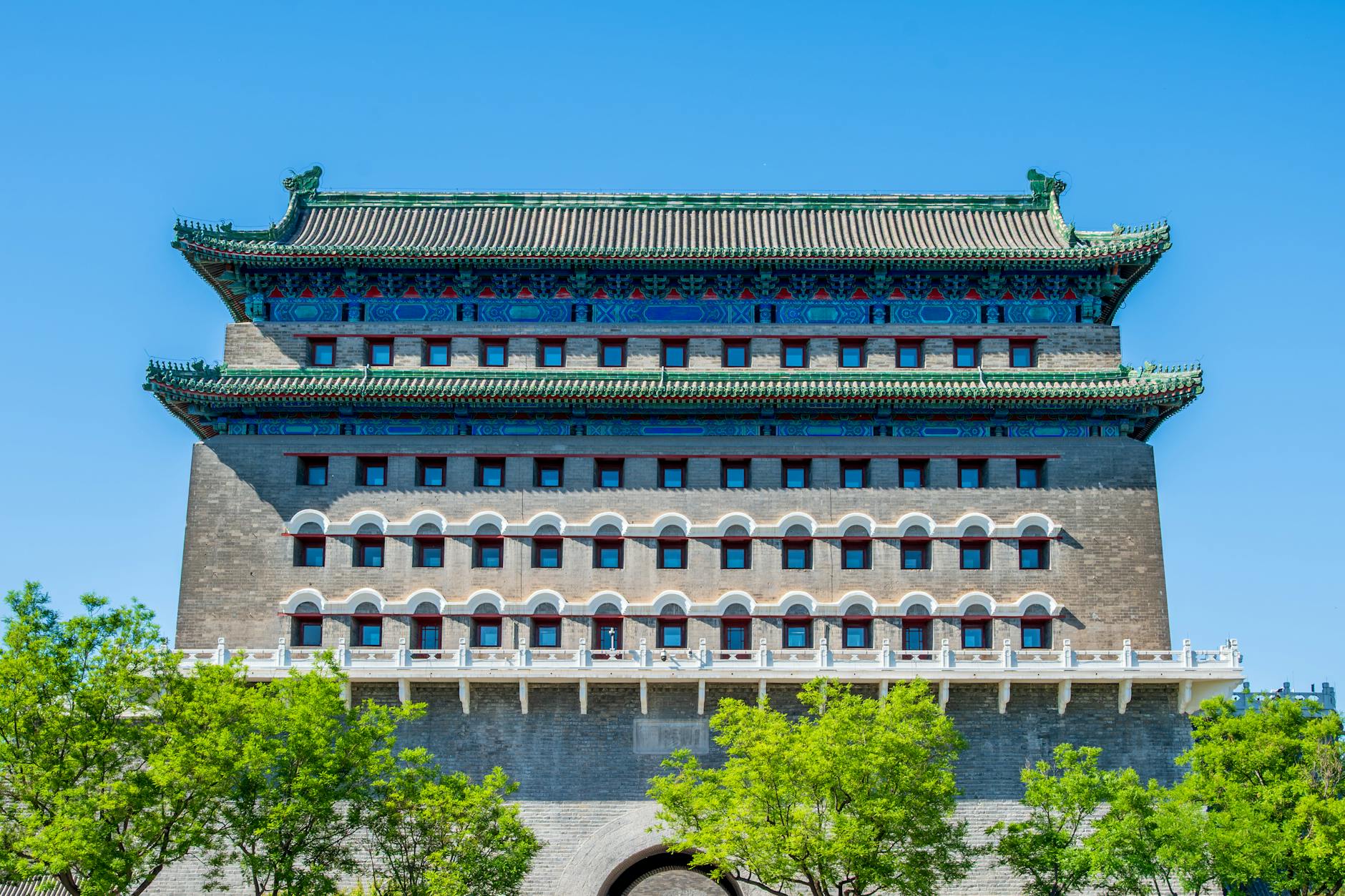 View of the iconic Zhengyangmen Gate Tower under a clear blue sky with vibrant green trees.