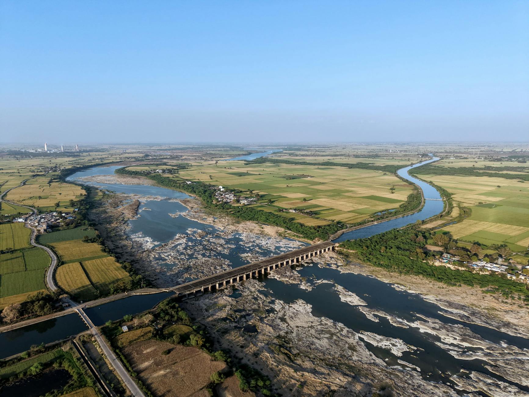 A stunning aerial shot of a river bridging lush green farmlands in India.