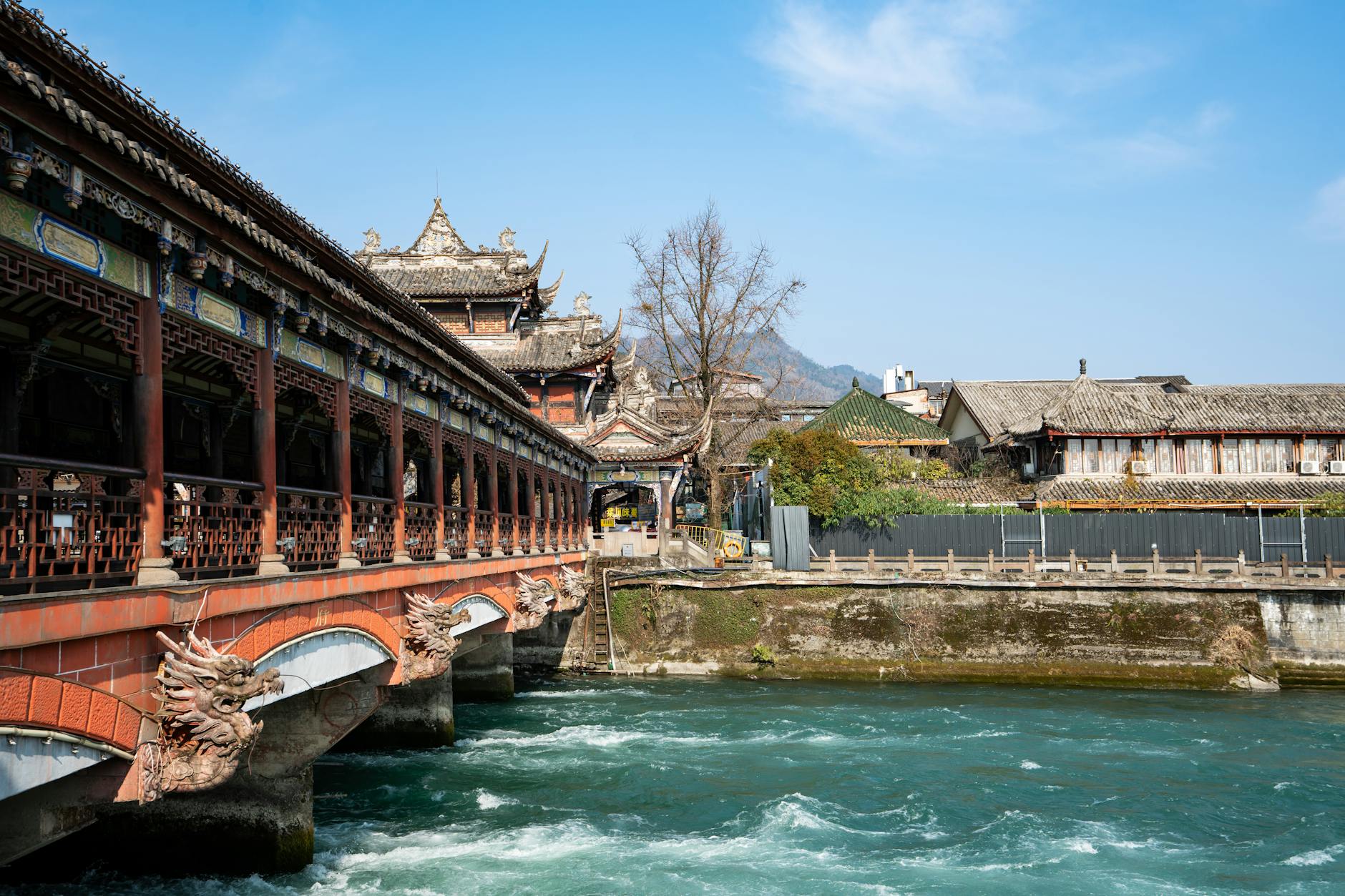 Scenic view of an ancient Chinese bridge with dragon carvings and architectural details over a river in bright daylight.