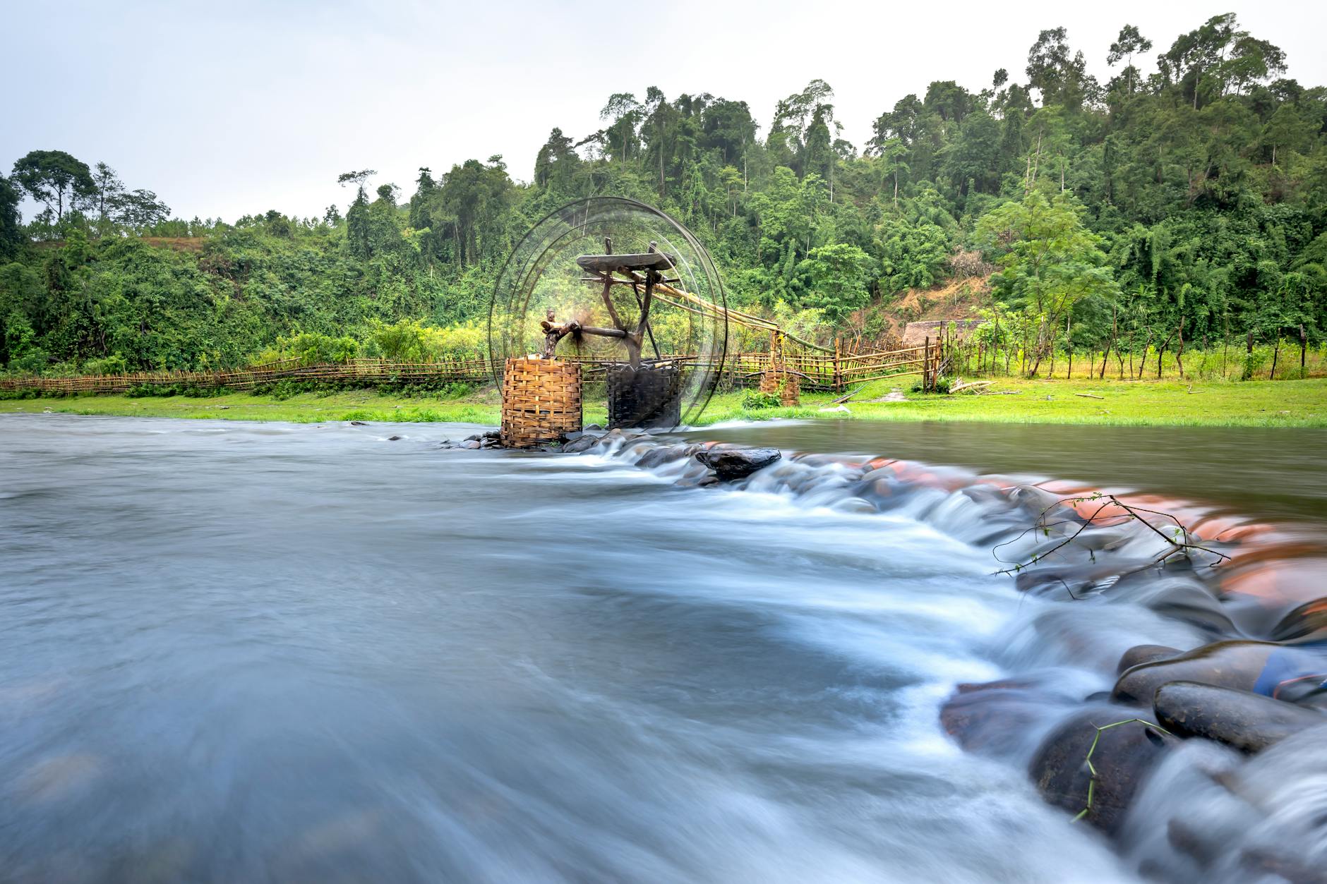 Peaceful river scene with lush forest and traditional water wheel for irrigation.
