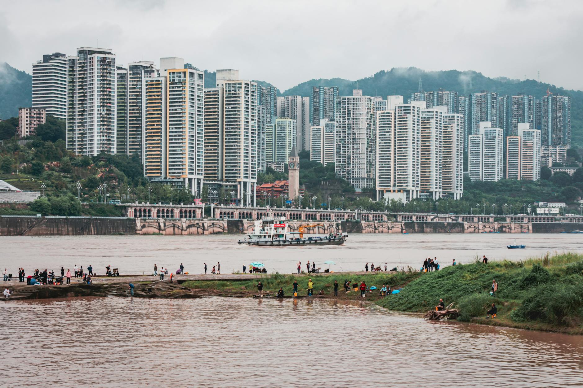 View of skyscrapers by river with people relaxing in the foreground.
