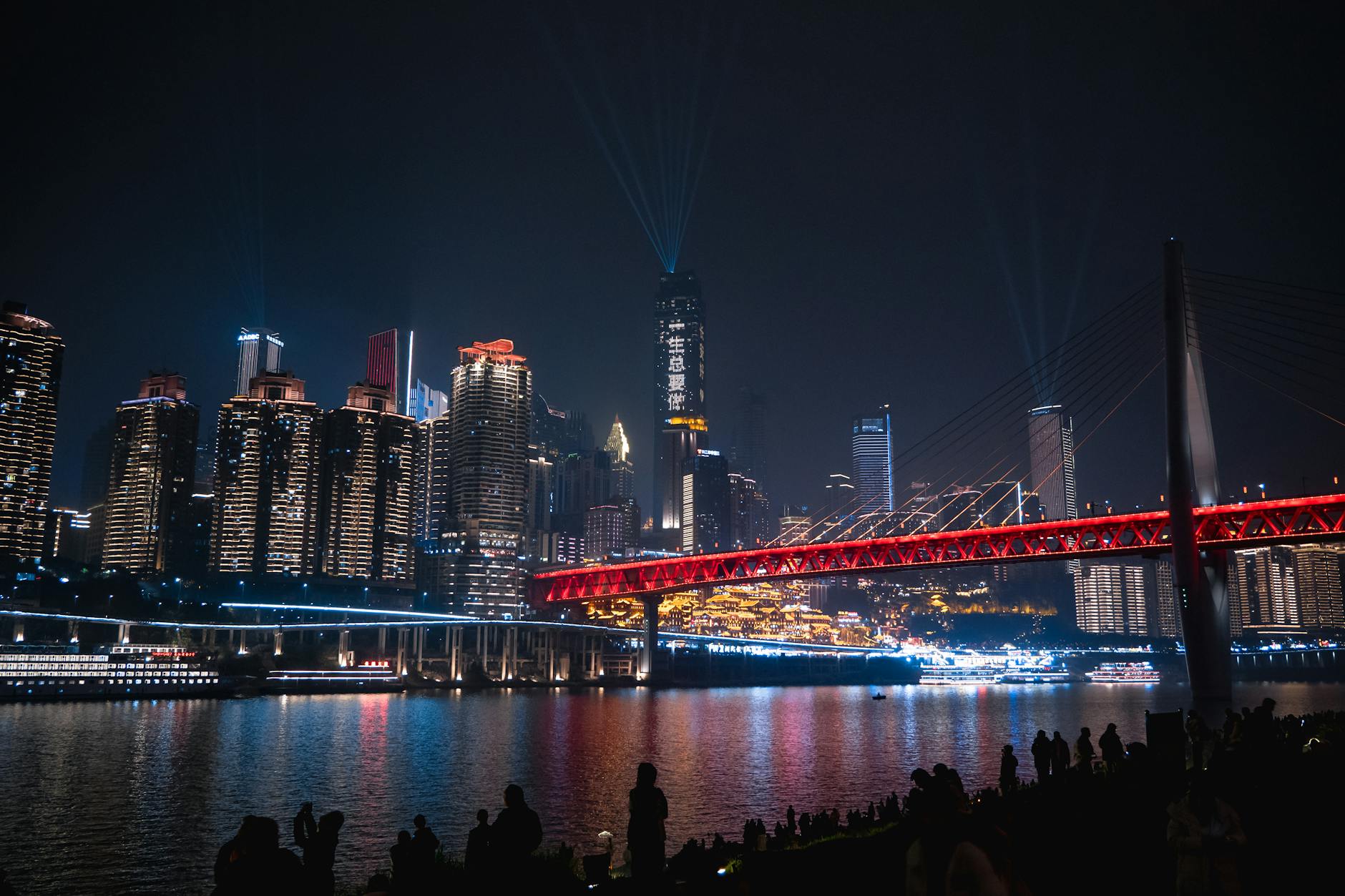Vibrant night view of Chongqing's skyline and illuminated bridge reflecting on the river.